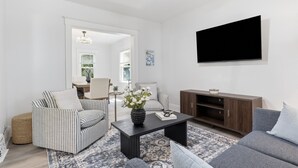 A living room with striped sofas, a coffee table, a flat-screen TV, and a wooden cabinet. - Historic 4BR Home Near South Wedge & Park Ave - Family Friendly with A/C (Rochester)