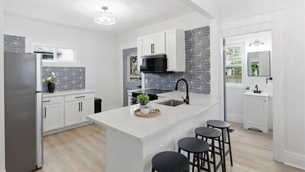 A modern kitchen with white cabinetry, a central island with stools, a black microwave, and a stainless steel refrigerator. - Historic 4BR Home Near South Wedge & Park Ave - Family Friendly with A/C (Rochester)