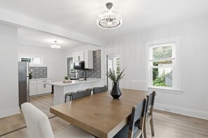 A modern kitchen with white cabinetry, a central island, and a dining area with a wooden table and chairs.