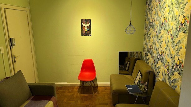 A living room with a red chair, a sofa, and a wall with a tropical print.