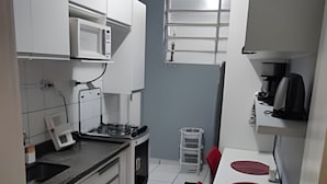 Cozinha compacta com armários brancos, micro-ondas, cafeteira e um pequeno espaço de refeições com cadeiras vermelhas.