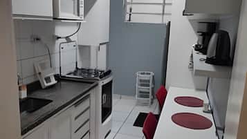 Cozinha compacta com armários brancos, micro-ondas, cafeteira e um pequeno espaço de refeições com cadeiras vermelhas.