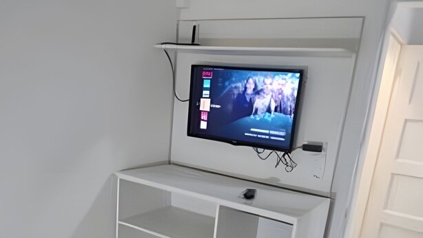 A room with a bed, a TV mounted on a white shelf, and a towel on the bed. - Quarto Individual Augusta Paulista Frei (São Paulo)
