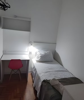 Una habitación pequeña y funcional con una cama individual, un escritorio y una silla.
