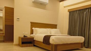 A hotel room with a bed, bedside table, and an air conditioning unit.