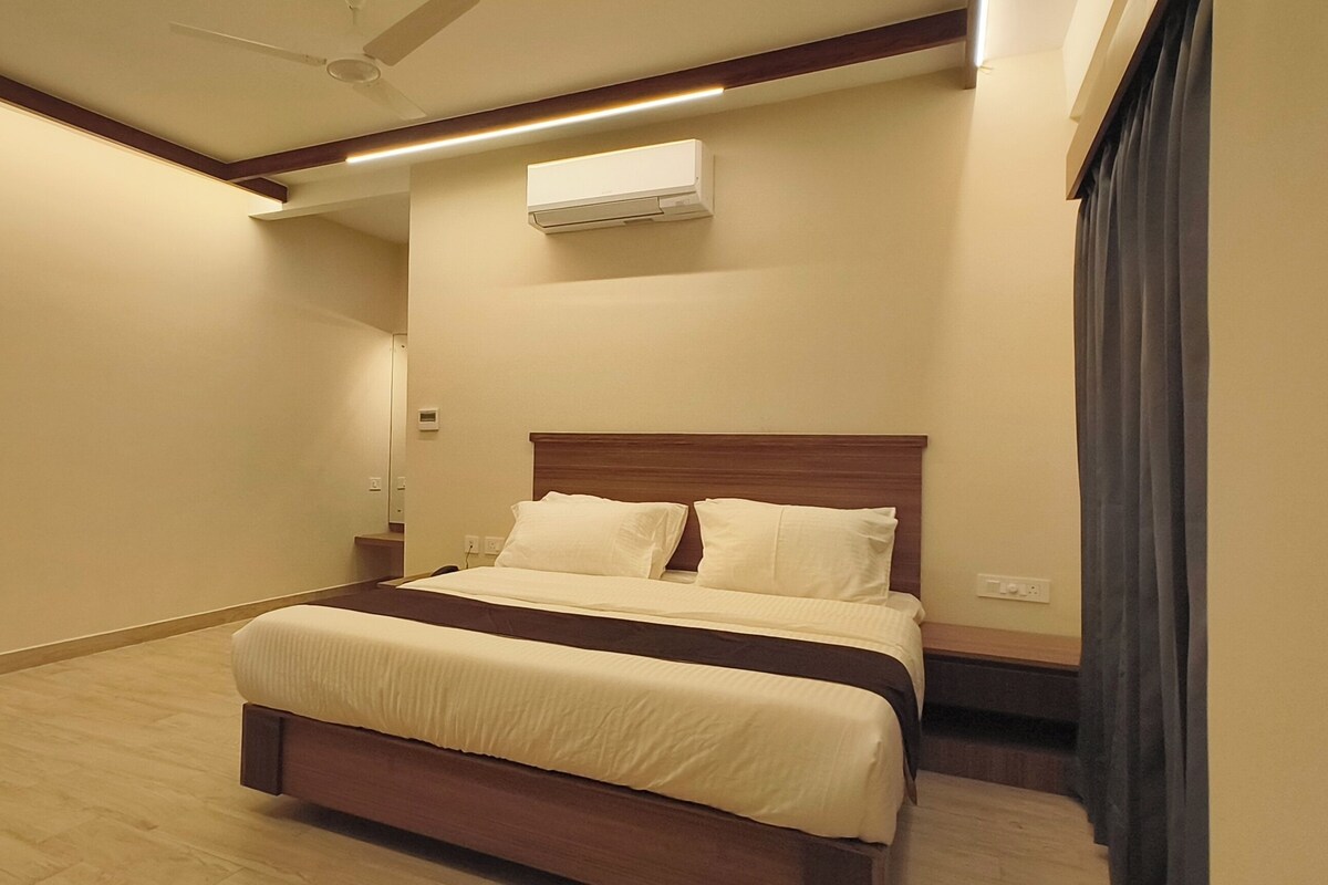 Habitació d'hotel amb un llit, un ventilador de sostre, un aire condicionat i una finestra amb cortines.