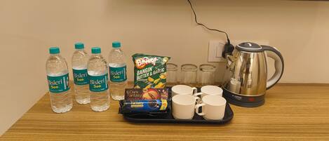 A table with water bottles, a coffee maker, mugs, and a snack package.