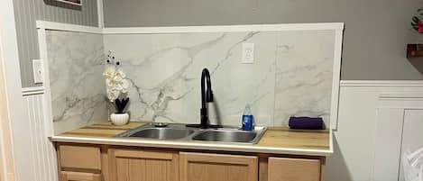 A compact kitchen with a marble backsplash, wooden cabinets, a black faucet, and a single flower vase.