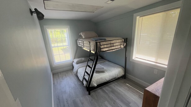 A bunk bed room with a window, a ceiling vent, and a wooden floor. - Adorable 2-bedroom house with AC in charming Lusby (Lusby)