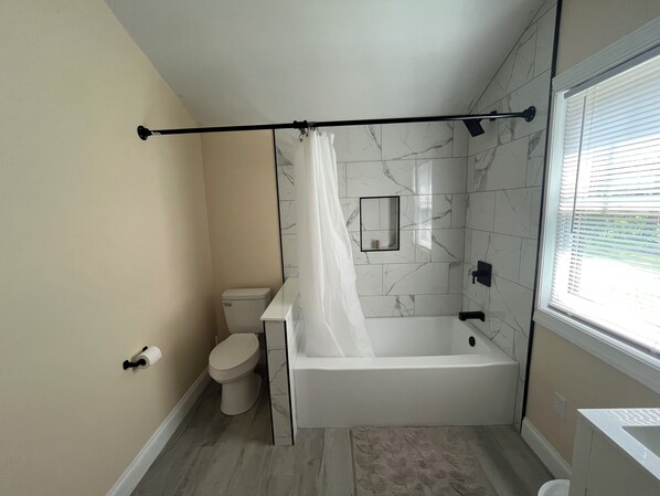 A bathroom with a toilet, a bathtub, and a shower curtain. - Adorable 2-bedroom house with AC in charming Lusby (Lusby)
