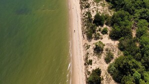 An aerial view of a coastal area with a beach, dense greenery, and a lighthouse. - Adorable 2-bedroom house with AC in charming Lusby (Lusby)