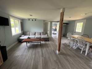 A spacious living room with a sectional sofa, a wooden coffee table, and a dining area with white chairs. - Adorable 2-bedroom house with AC in charming Lusby (Lusby)