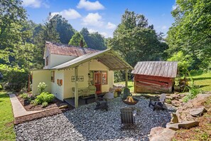 Une cabane rustique dotée d’une terrasse en gravier, de meubles d’extérieur et d’un petit abri de jardin.