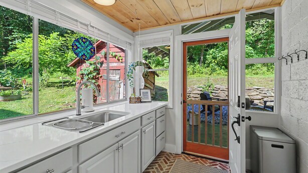 A kitchen with white cabinets, a sink, and a window overlooking a garden. - Ruby's Coop (Bryson City)