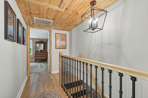 Un escalier en bois avec une rampe noire, un plafond en bois et un luminaire.