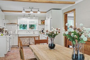 A kitchen with white cabinets, a wooden dining table, and a vase with flowers. - Ruby's Coop (Bryson City)