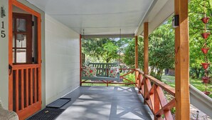 A covered porch with a wooden railing, a bench with a floral cushion, and a view of a garden. - Ruby's Coop (Bryson City)