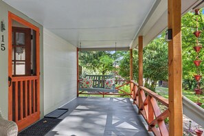 Eine überdachte Veranda mit Holzgeländer, eine Bank mit floralem Sitzkissen und Blick auf einen Garten.