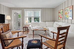 Ein Wohnzimmer mit einem weißen Sofa, Holzstühlen, einem Fernseher und einem kleinen Tisch.