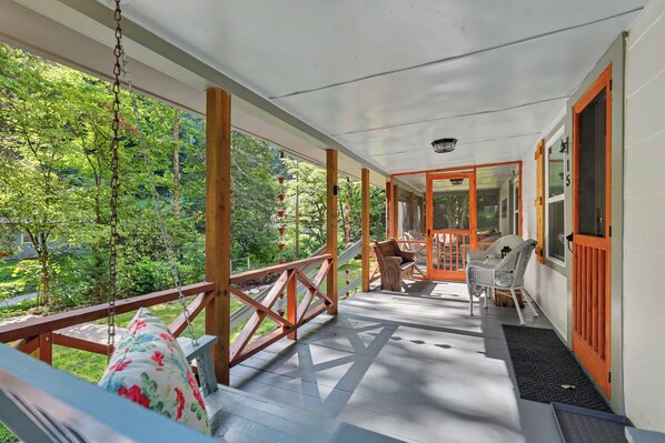 Une véranda couverte avec une balustrade en bois, un banc et une chaise.