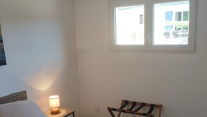 A bedroom with a bed, a nightstand with a lamp, a chair, and a window. - The garleche (Sainte-Eulalie-en-Born)