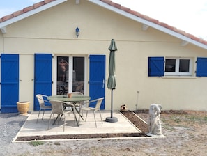 A house with a patio, a table with chairs, a green umbrella, and a statue.
