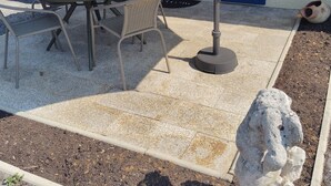 An outdoor patio with a table and chairs, a stone sculpture, and a blue garage door. - The garleche (Sainte-Eulalie-en-Born)