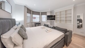A modern hotel room with a large bed, a sofa, a TV mounted on the wall, and a small desk. - Comfort Studio by Harrods (London)