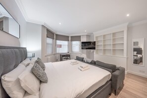 A modern hotel room with a large bed, a sofa, a TV mounted on the wall, and a small desk. - Comfort Studio by Harrods (London)