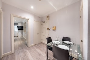 A modern dining area with a glass table, black chairs, and white plates. - Comfort Studio by Harrods (London)