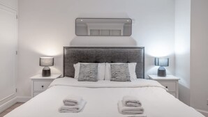A modern bedroom with a large bed, two bedside tables, a headboard, and a mirror above the bed. - Comfort Studio by Harrods (London)