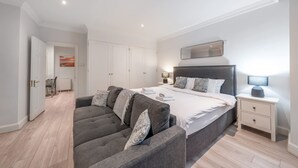 A modern bedroom with a large bed, bedside tables, a sofa, and a view of the sky. - Comfort Studio by Harrods (London)