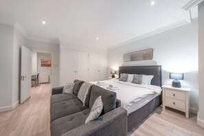 A modern bedroom with a large bed, bedside tables, a sofa, and a view of the sky. - Comfort Studio by Harrods (London)