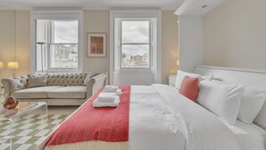 A hotel room with a bed, a sofa, a window with a city view, and a checkered floor. - Bright Studio in Belgravia With Views (London)