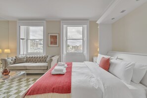 Ein Hotelzimmer mit Bett, einer Couch, einem Fenster mit Blick auf die Stadt und einem karierten Boden.