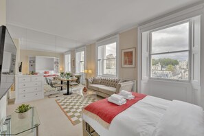 Ein modernes Hotelzimmer mit Bett, Sofa, Essbereich und Blick auf die Stadt.