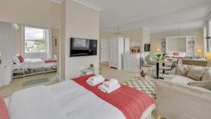 A hotel room with a large bed, a TV, a desk with a chair, a sofa, and a dining table with chairs. - Bright Studio in Belgravia With Views (London)
