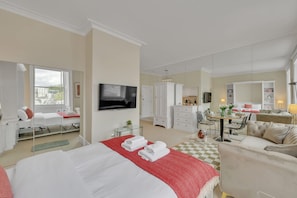 Ein Hotelzimmer mit einem großen Bett, einem Fernseher, einem Schreibtisch mit Stuhl, einer Couch und einem Esstisch mit Stühlen.