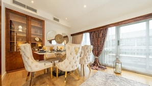 A dining area with a round table, four upholstered chairs, and a large window with curtains. - Spacious Penthouse Near Hyde Park London (London)