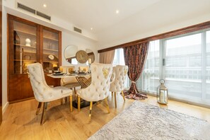 A dining area with a round table, four upholstered chairs, and a large window with curtains. - Spacious Penthouse Near Hyde Park London (London)