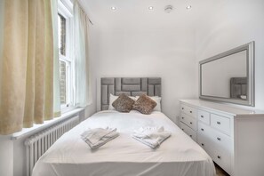 A bedroom with a bed, a dresser, a mirror, and a window with curtains. - Contemporary 1B Apartment - Paddington St (London)