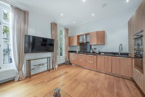 A modern kitchen with wooden cabinets, a built-in oven, and a large window with curtains. - Contemporary 1B Apartment - Paddington St (London)
