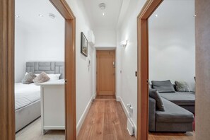 A narrow hallway leading to two bedrooms with a bed, a bedside table, and a nightstand in each room. - Contemporary 1B Apartment - Paddington St (London)