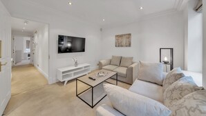 A modern living room with a flat-screen TV, a sofa, a coffee table, and a TV stand. - Charming 2-bedroom Apartment in Knightsbridge (London)