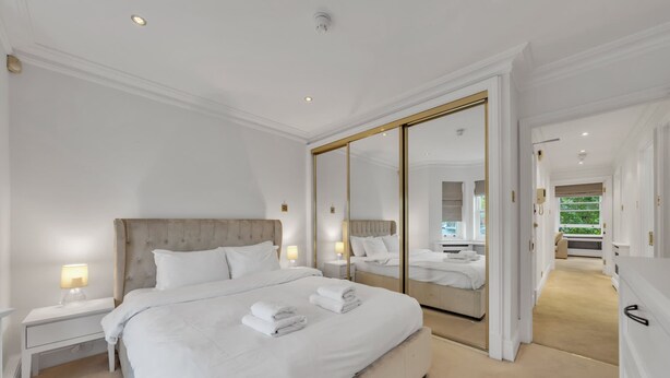 A hotel room with a large bed, a mirror, a nightstand, and a view of the garden. - Charming 2-bedroom Apartment in Knightsbridge (London)