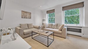 A modern living room with two sofas, a coffee table, a vase with flowers, and a painting on the wall. - Charming 2-bedroom Apartment in Knightsbridge (London)