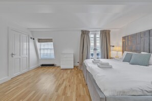 A hotel room with a large bed, a wardrobe, a window with curtains, and a radiator. - Charming Mayfair Home With Modern Comforts (London)