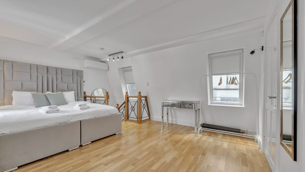 A modern bedroom with a large bed, a bedside table, a radiator, and a window with clothes hanging. - Charming Mayfair Home With Modern Comforts (London)