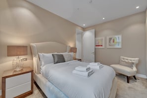 Ein modernes Schlafzimmer mit einem großen Bett, Nachttischen, einem Sessel und Kunstwerken an den Wänden.