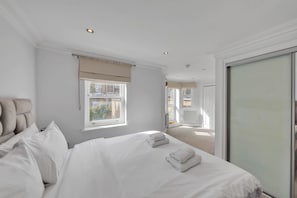 A hotel room with a large bed, a window with curtains, a door leading to another room, and a view of the outside. - Luxury 3-bedroom Apartment Next to Harrods (London)